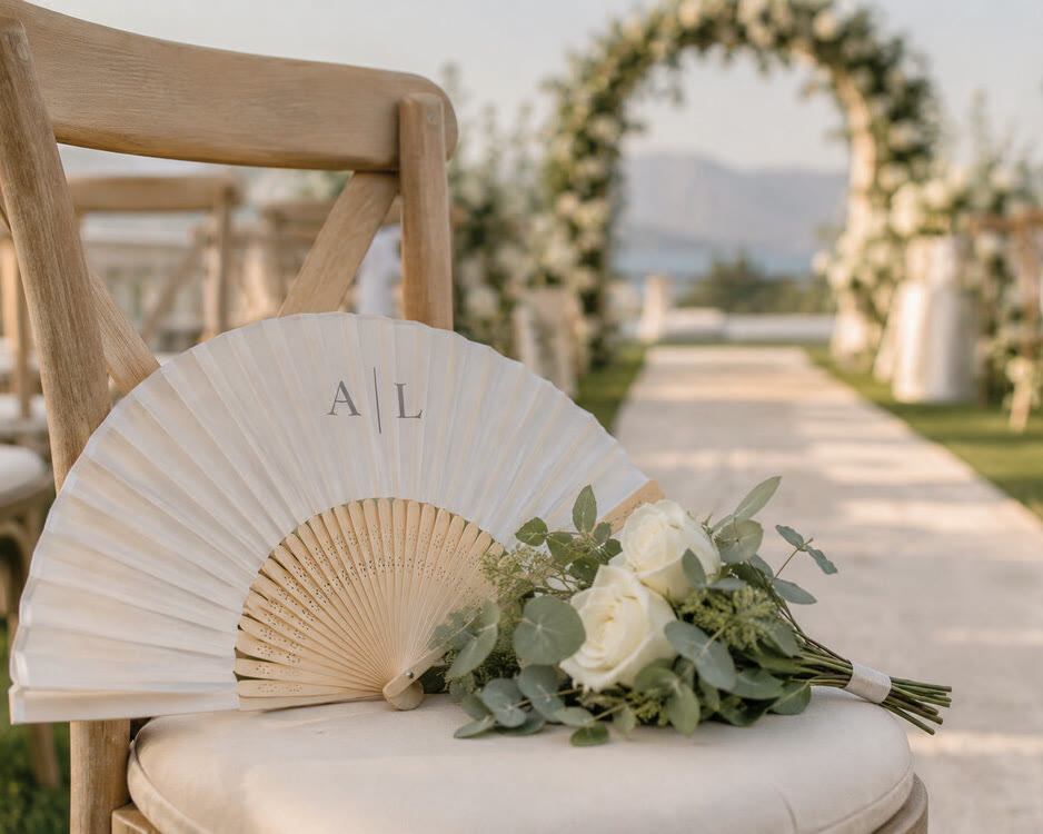 Abanico de bambú blanco con monograma impreso, en una silla de ceremonia de boda